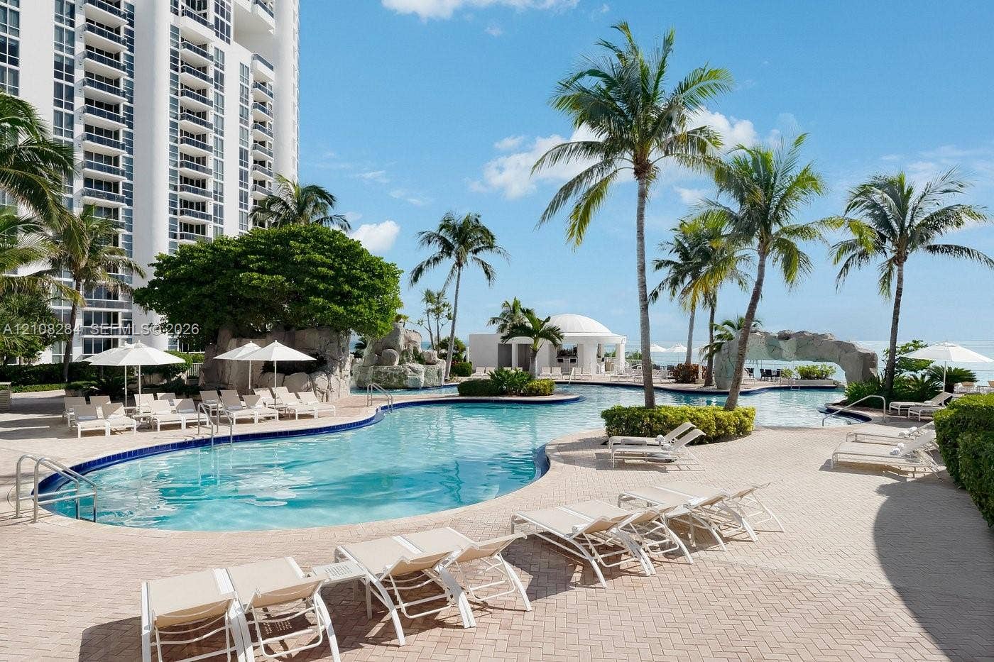 18001 Collins Avenue, #908, Sunny Isles Beach, FL 33160 Resort-style swimming pool featuring rock waterfall features, paver decking, and integrated landscaping