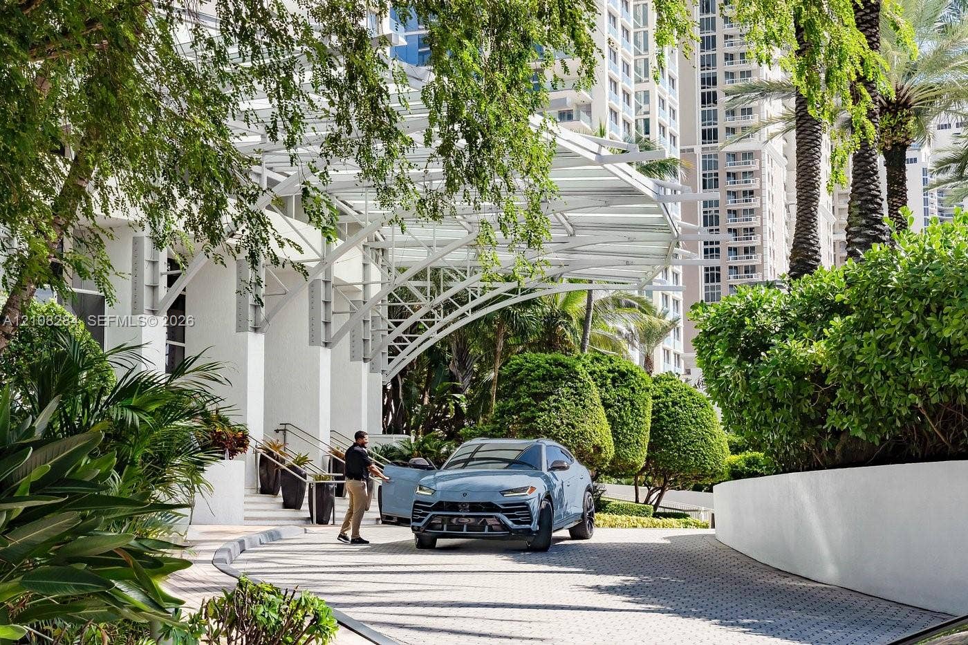 18001 Collins Avenue, #908, Sunny Isles Beach, FL 33160 Porte-cochere entrance featuring white structural steel framing, paved circular driveway, and mature perimeter landscaping