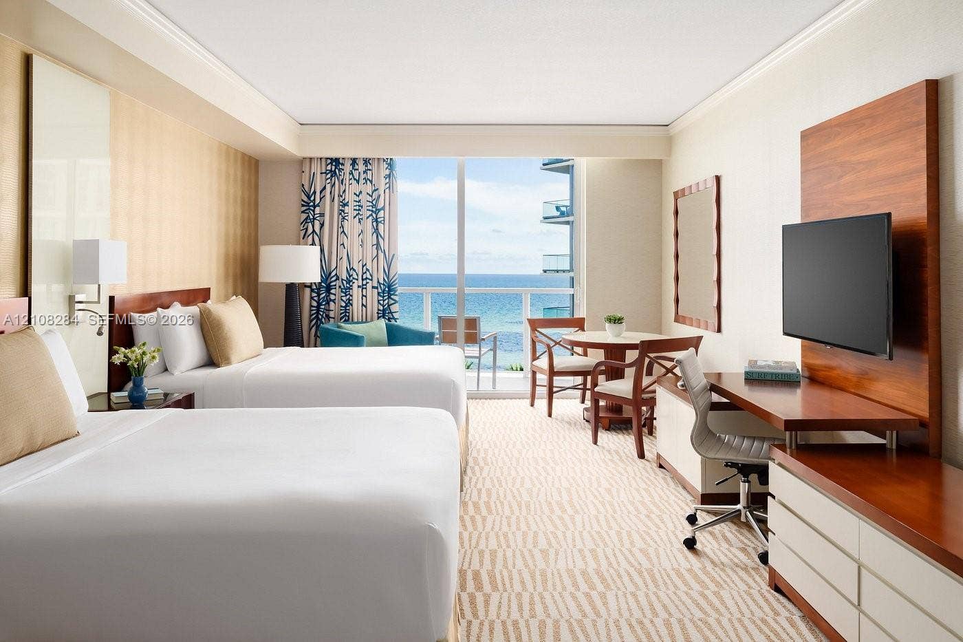18001 Collins Avenue, #908, Sunny Isles Beach, FL 33160 Floor-to-ceiling glass sliding doors opening to an exterior balcony, ocean backdrop, built-in wood-finish media console, integrated desk workspace, and recessed tray ceiling