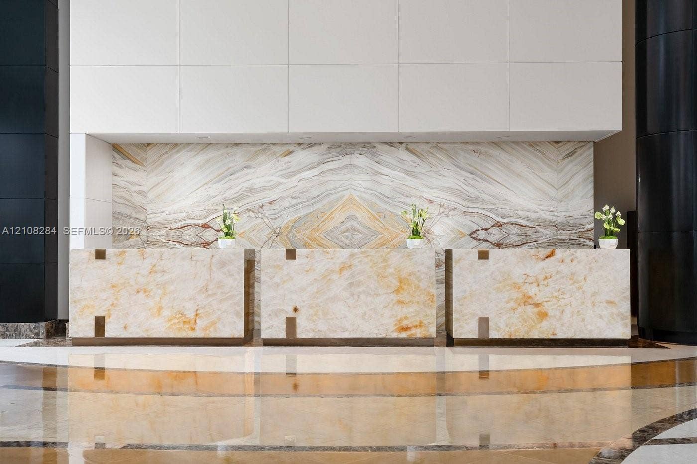 18001 Collins Avenue, #908, Sunny Isles Beach, FL 33160 Reception desk featuring stone paneling with book-matched detailing, polished natural stone flooring, and contrasting matte black architectural columns