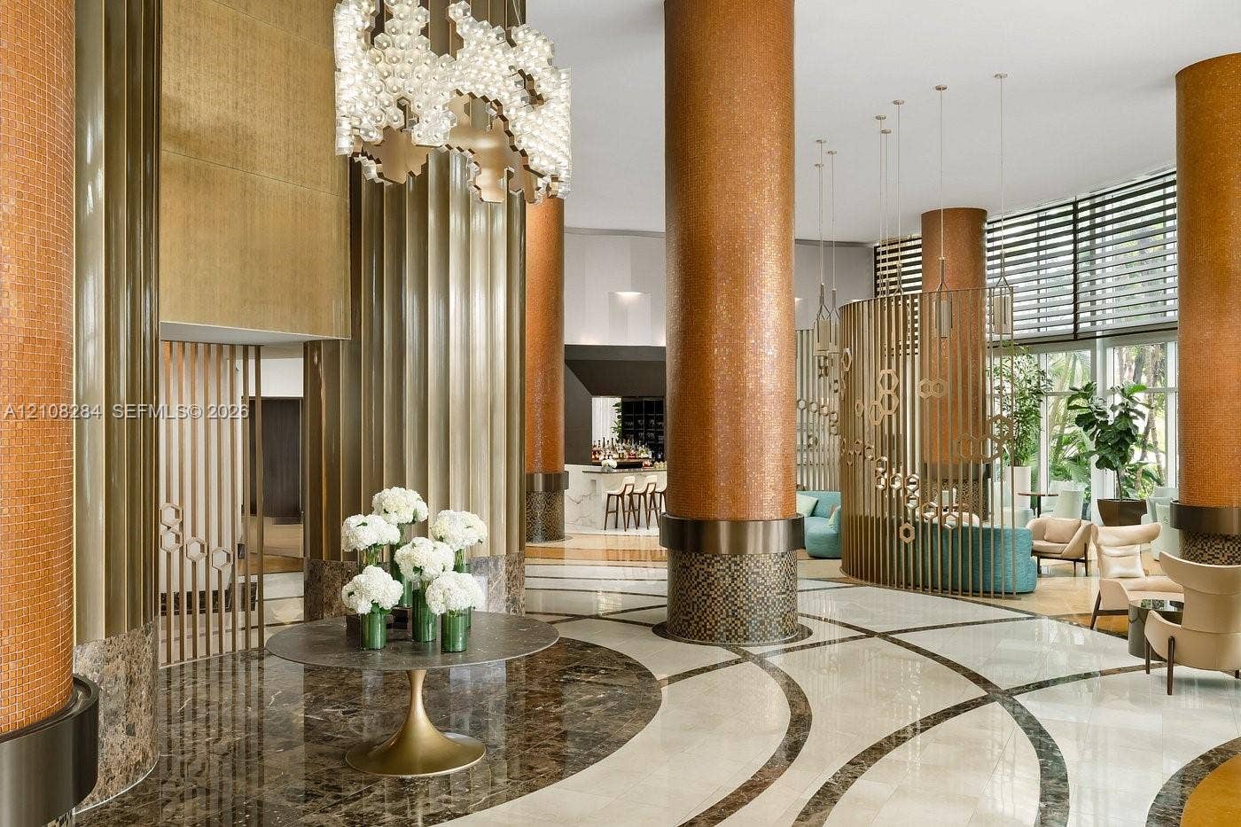 18001 Collins Avenue, #908, Sunny Isles Beach, FL 33160 Grand lobby featuring polished stone flooring with inlaid patterns, metallic-finished structural columns, decorative vertical screening, and tiered custom chandelier lighting