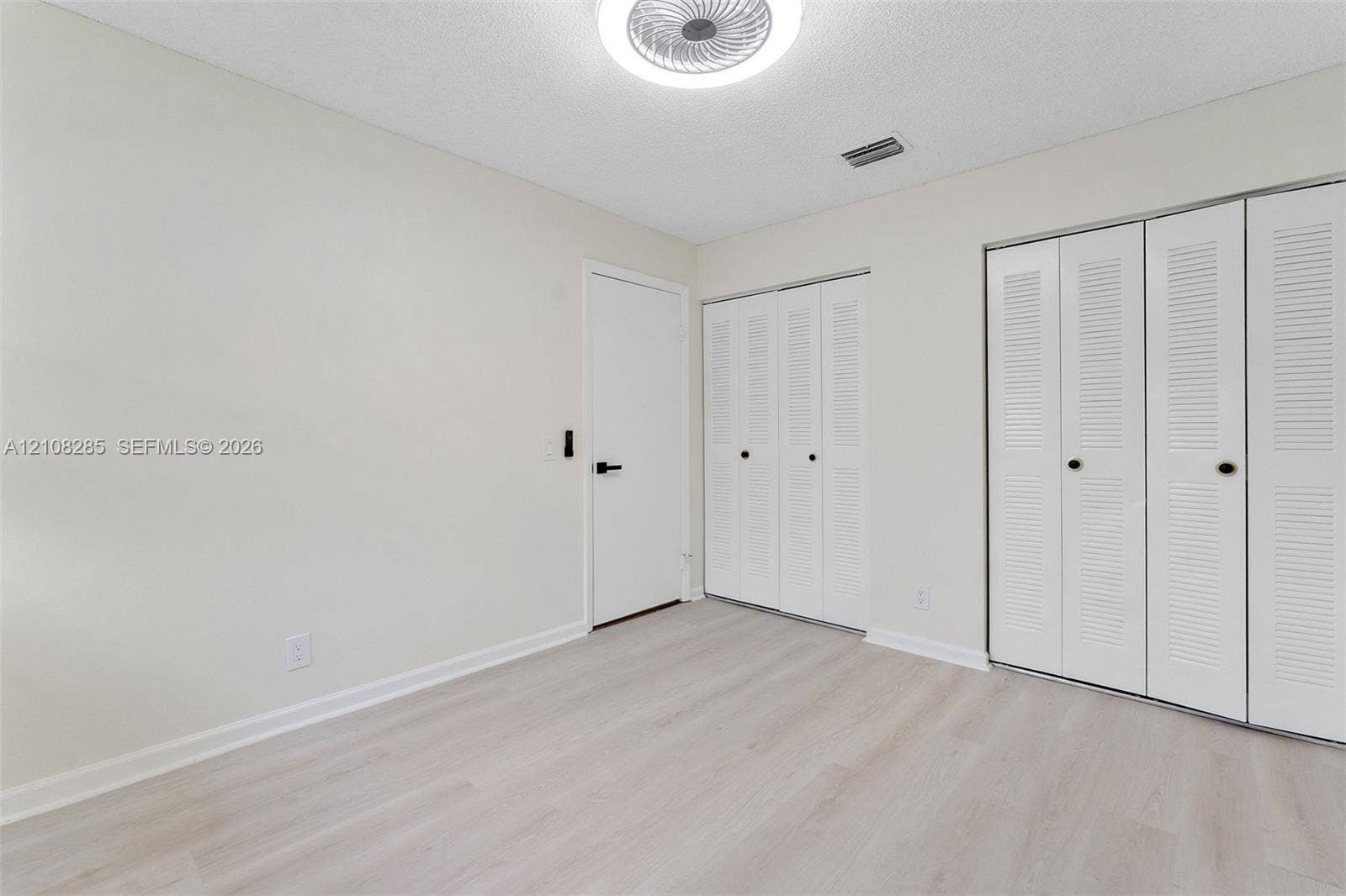 6626 Via Regina, #0, Boca Raton, Boca Raton, FL 33433 Neutral-toned room featuring wood-finish flooring, dual closets with louvered doors, and a central circular flush-mount ceiling light