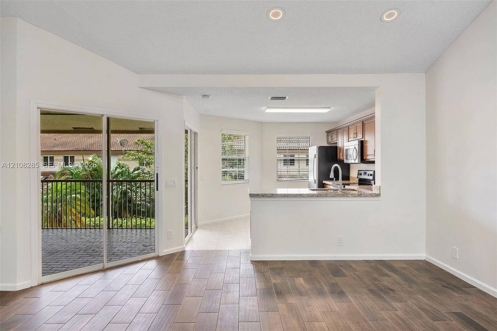 6626 Via Regina, #0, Boca Raton, Boca Raton, FL 33433 Open-concept space featuring wood-finish flooring, recessed lighting, a kitchen pass-through with a stone-finish countertop, and sliding glass doors with exterior balcony access