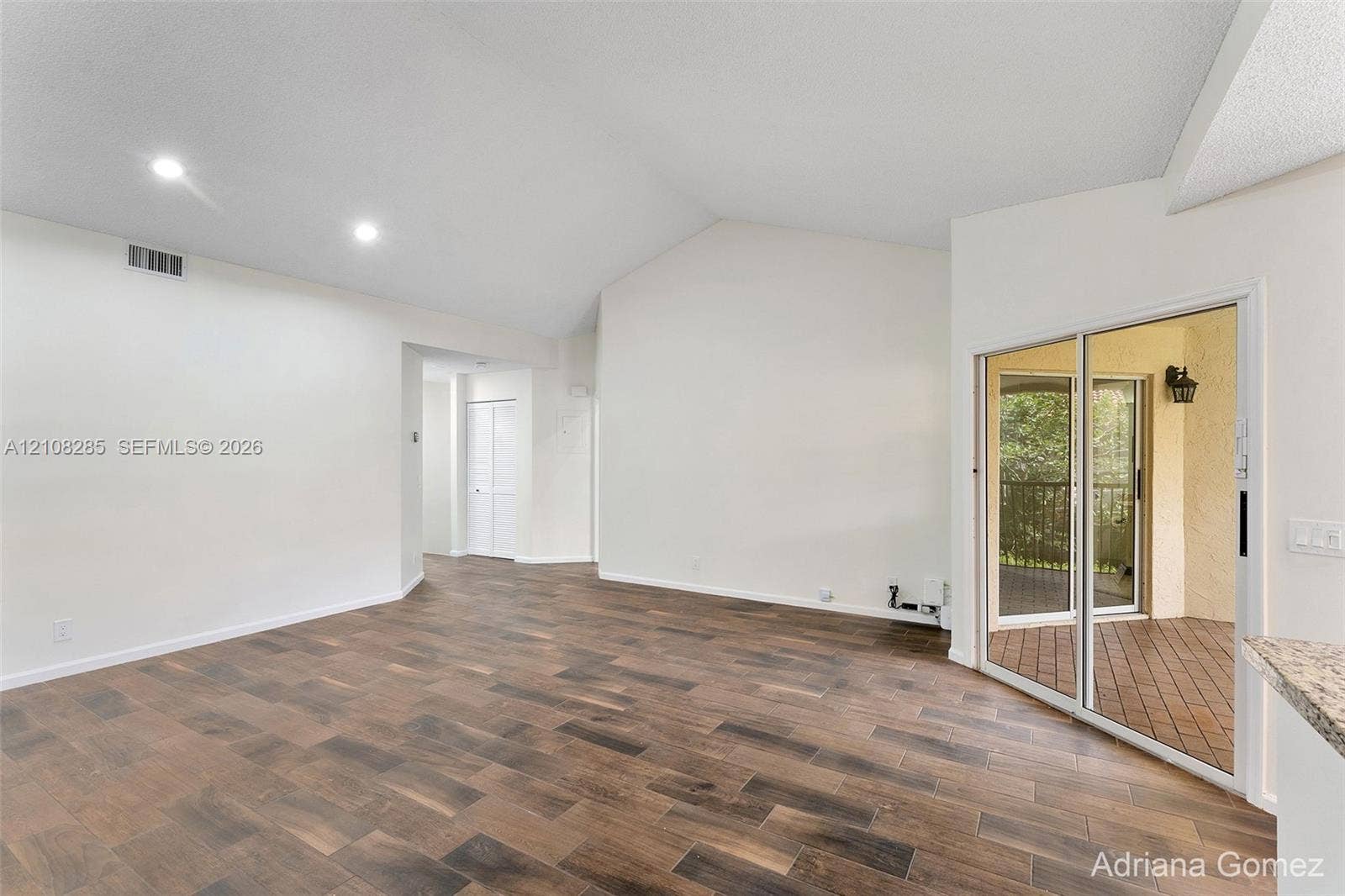 6626 Via Regina, #0, Boca Raton, Boca Raton, FL 33433 Interior space featuring vaulted ceilings, recessed lighting, and wood-finish flooring, with a glass sliding door providing access to a covered outdoor balcony