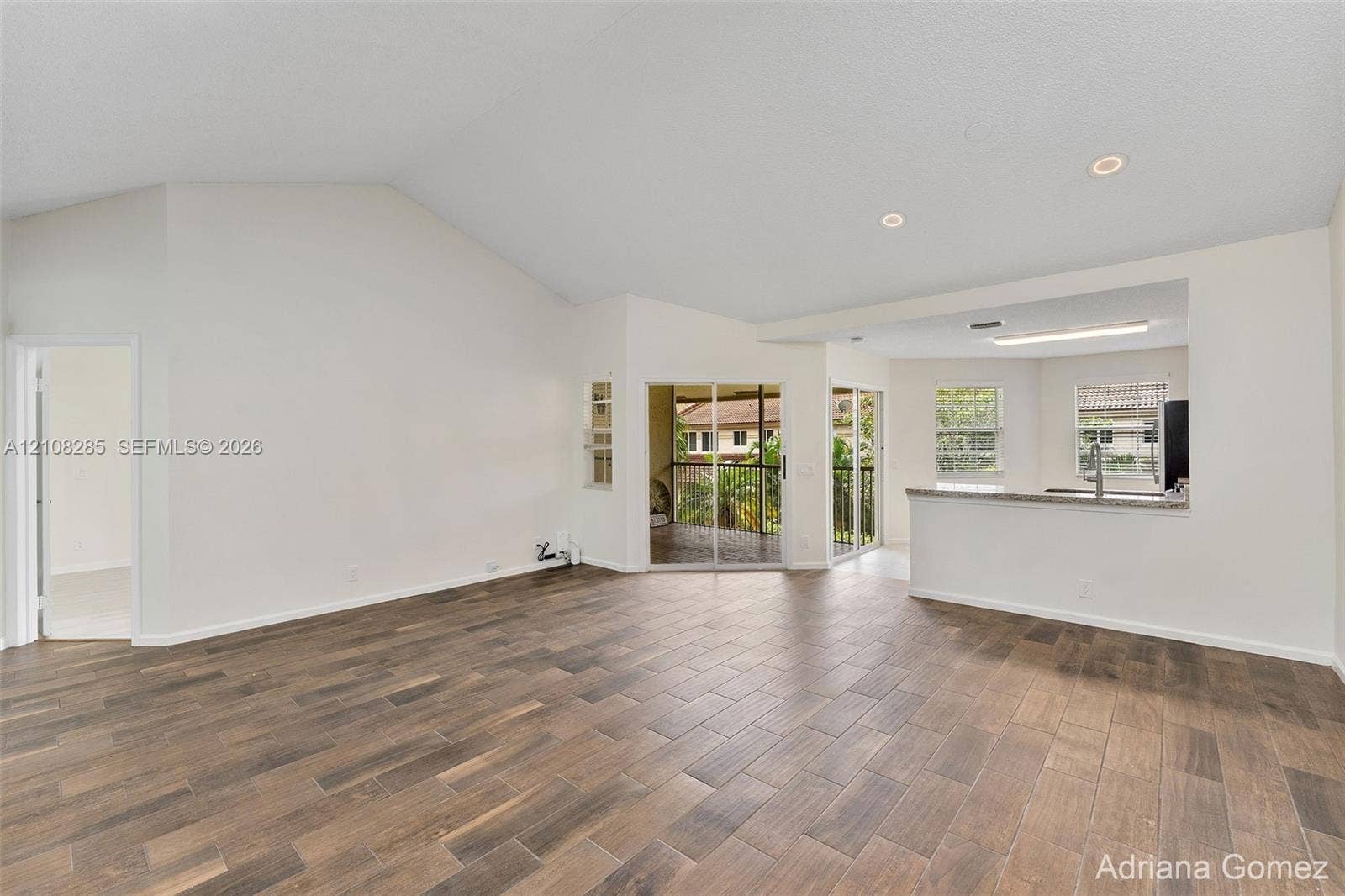 6626 Via Regina, #0, Boca Raton, Boca Raton, FL 33433 Vaulted ceilings, wood-finish tile flooring, recessed lighting, and sliding glass doors leading to a balcony, complemented by a kitchen pass-through with a stone-top breakfast bar