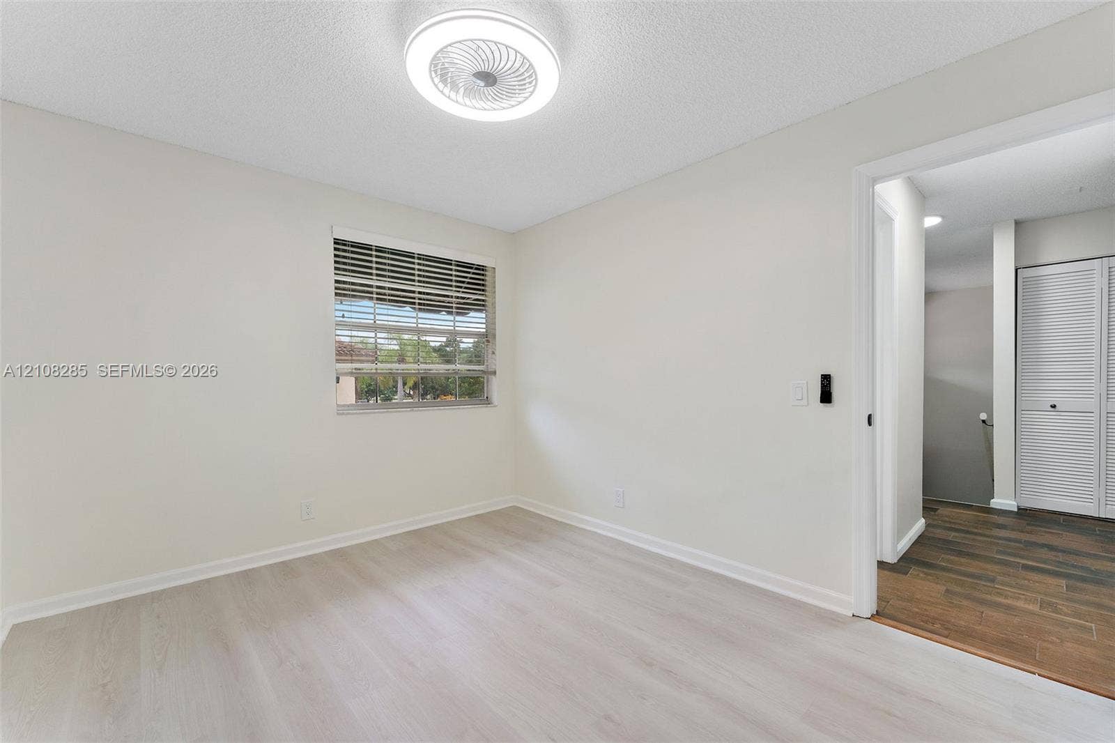 6626 Via Regina, #0, Boca Raton, Boca Raton, FL 33433 Interior space featuring neutral wall paint, wood-finish flooring, a recessed window with horizontal blinds, and a circular LED flush-mount ceiling fixture