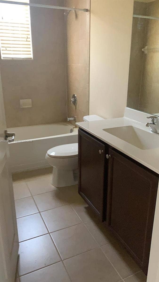 Bathroom featuring a vanity with dark-finish cabinetry, a light-toned countertop with an integrated basin, tile flooring, and a tiled shower-tub combination