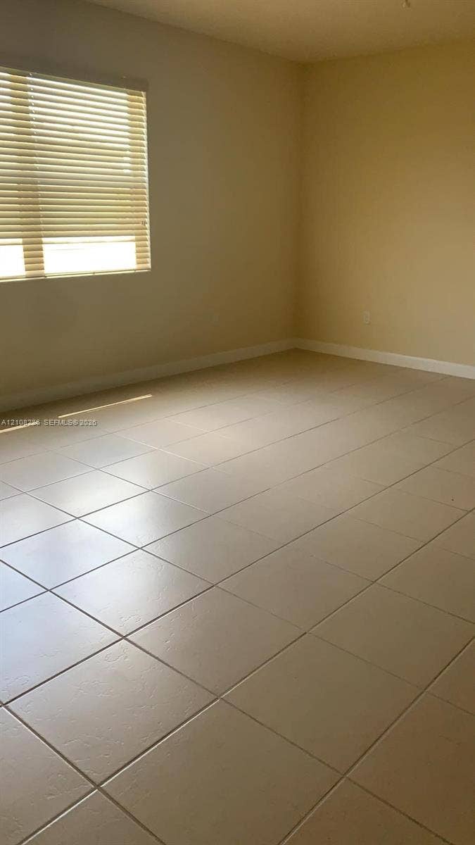 Neutral-toned ceramic tile flooring, horizontal window blinds, and solid-colored walls