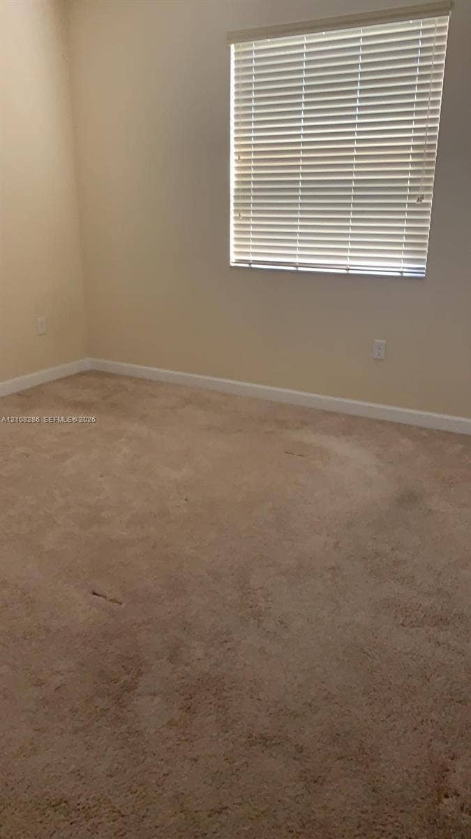 Neutral-toned interior space featuring carpeting and a window equipped with horizontal blinds