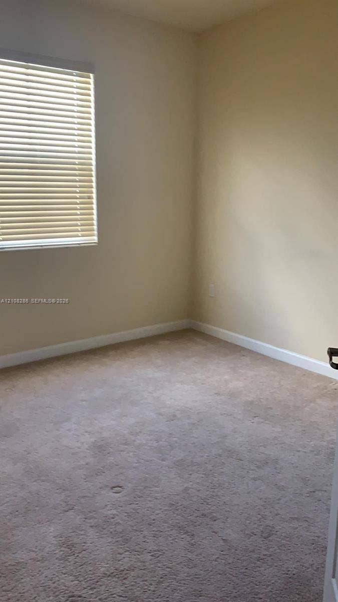 Neutral interior featuring wall-to-wall carpeting and a single window with horizontal blinds