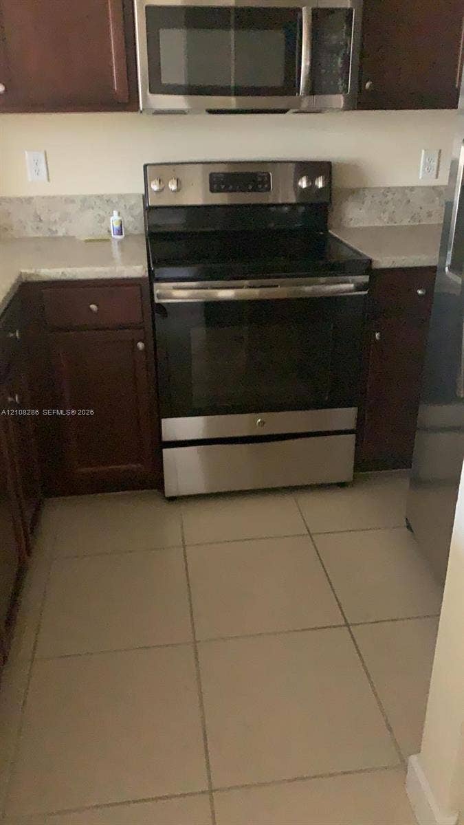 Kitchen featuring dark-finish cabinetry, neutral-toned countertops, tile flooring, and stainless steel appliances including an electric range and built-in microwave