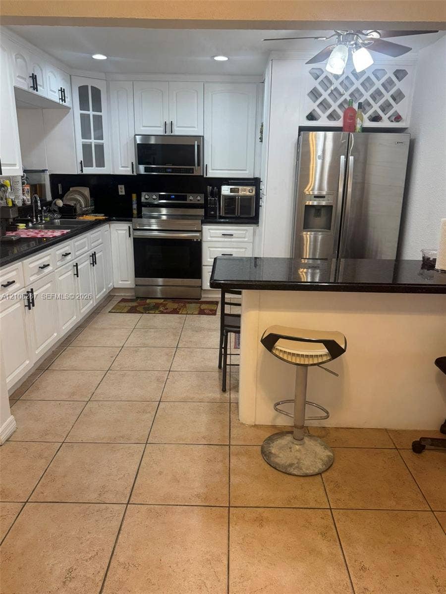 5350 NW 183rd Street, Miami Gardens, FL 33055 Kitchen featuring white shaker-style cabinetry, black stone countertops, stainless steel appliances, built-in wine storage, and ceramic tile flooring