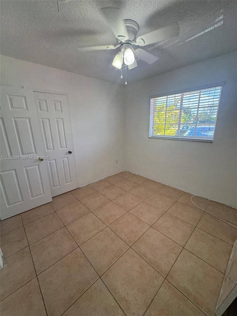 5350 NW 183rd Street, Miami Gardens, FL 33055 Interior space featuring ceramic tile flooring, a multi-pane window with horizontal blinds, double-door closet storage, and a ceiling-mounted fan with light fixture