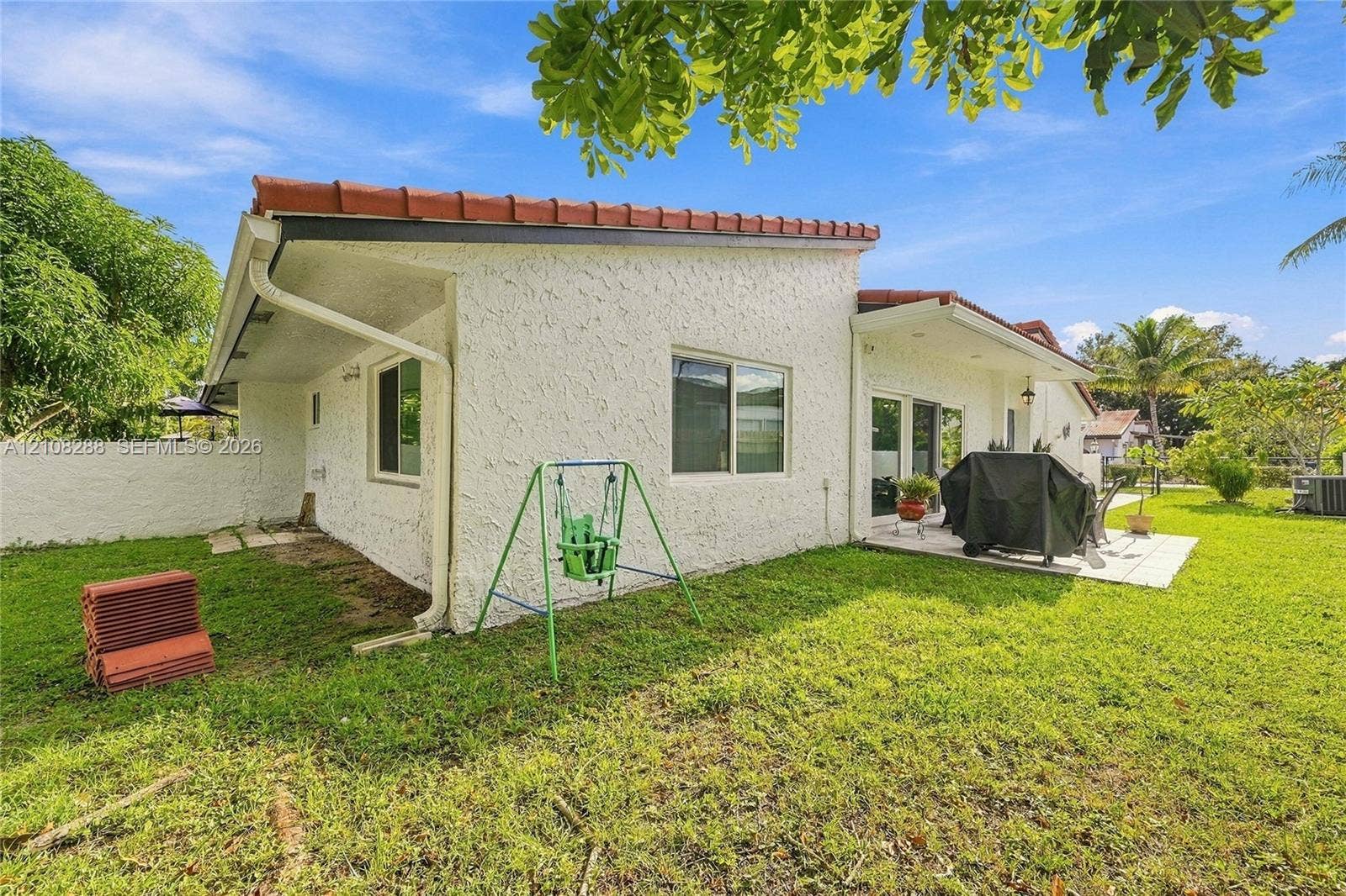 8292 NW 36th Street, Sunrise, FL 33351 Exterior featuring stucco siding, a low-slope roof with clay tiles, a concrete patio, and an expansive lawn