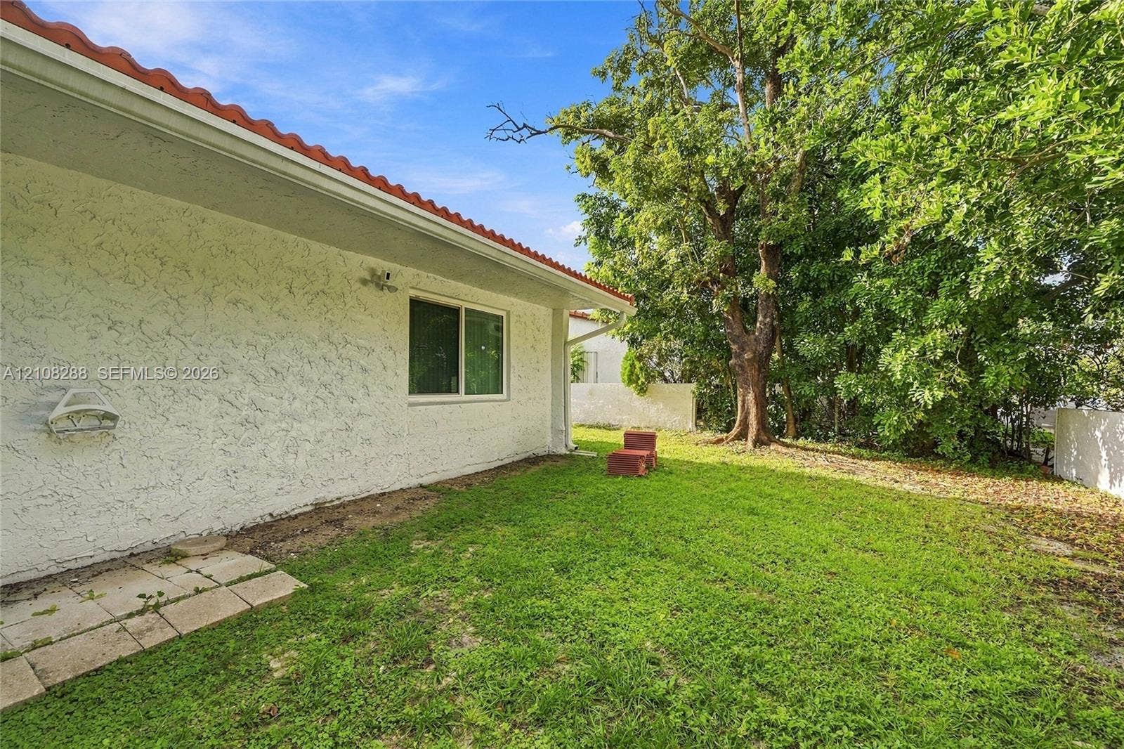 8292 NW 36th Street, Sunrise, FL 33351 Exterior side yard featuring textured stucco walls, a red-tile roof, a single-pane sliding window, and mature trees