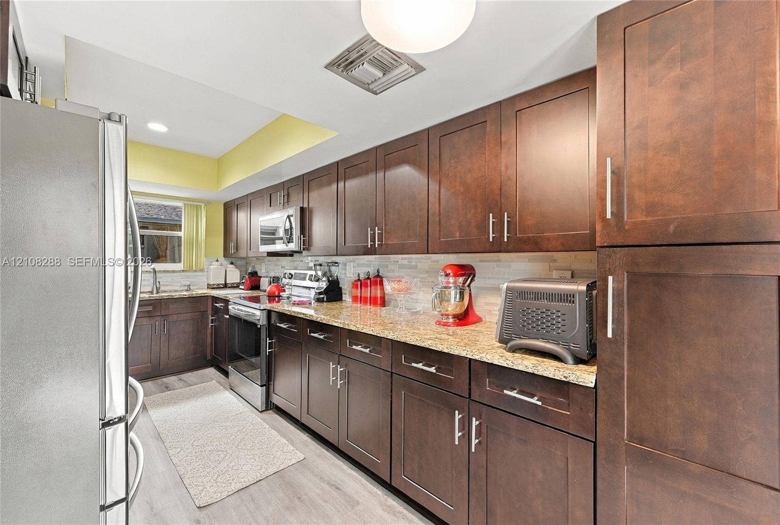 8292 NW 36th Street, Sunrise, FL 33351 Kitchen featuring dark wood-finish cabinetry, stone-style countertops, stainless steel appliances, and a light-toned tile backsplash
