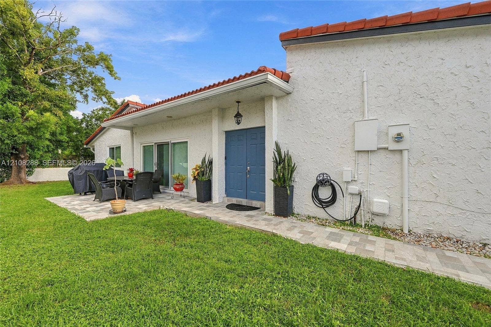 8292 NW 36th Street, Sunrise, FL 33351 Stucco exterior featuring a dual-tone tile roof, blue double entry doors, and expansive paver patio hardscaping