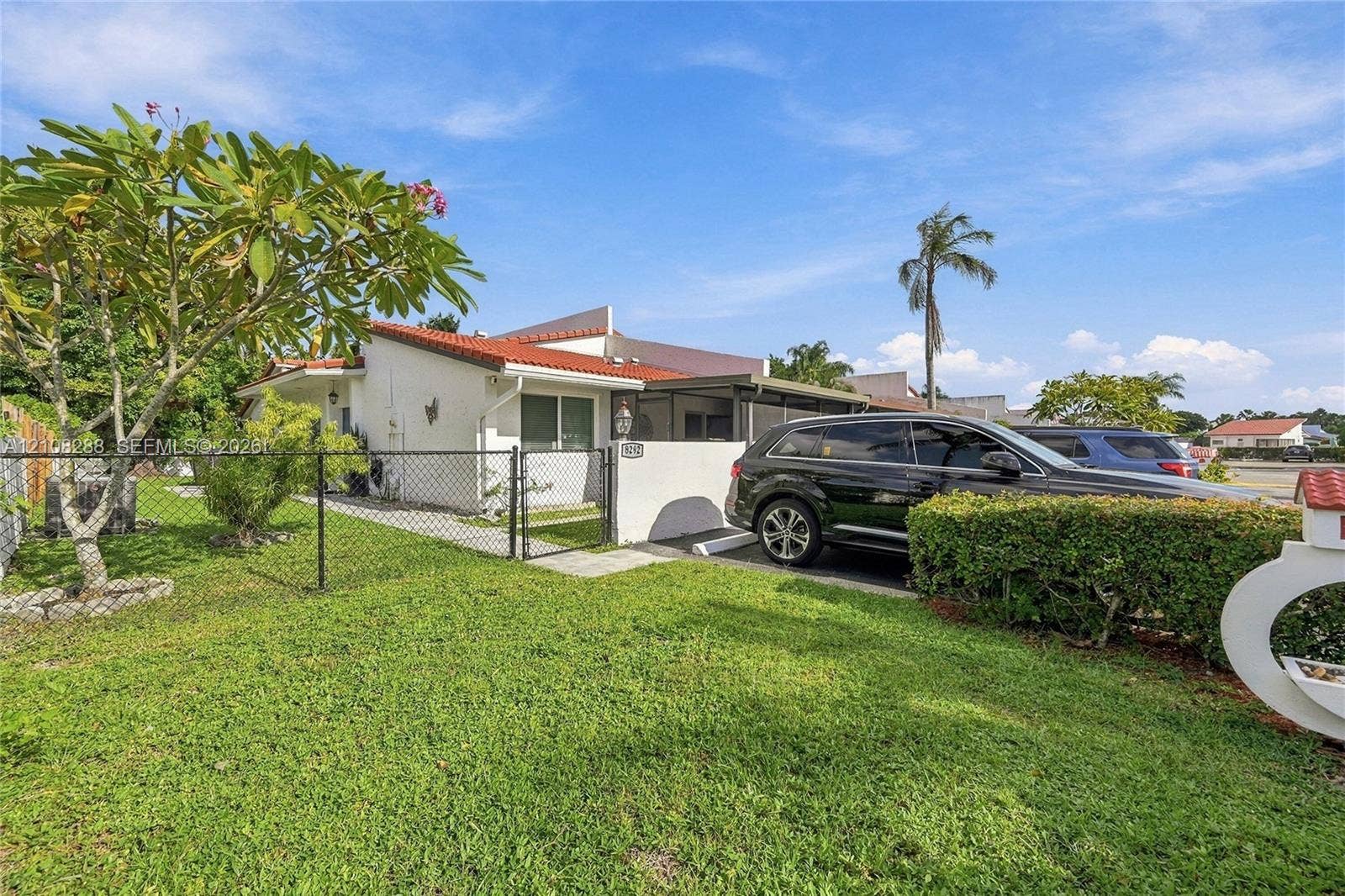 8292 NW 36th Street, Sunrise, FL 33351 Stucco exterior featuring a terracotta-tiled roof, covered parking structure, fenced front yard, and landscaped grounds