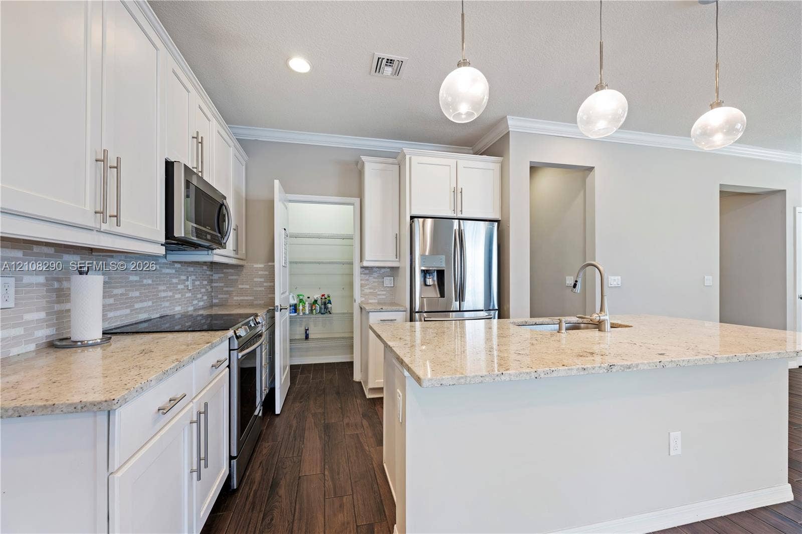 Kitchen featuring white shaker-style cabinetry, stone countertops, stainless steel appliances, wood-finish flooring, and three glass pendant lights over the central island