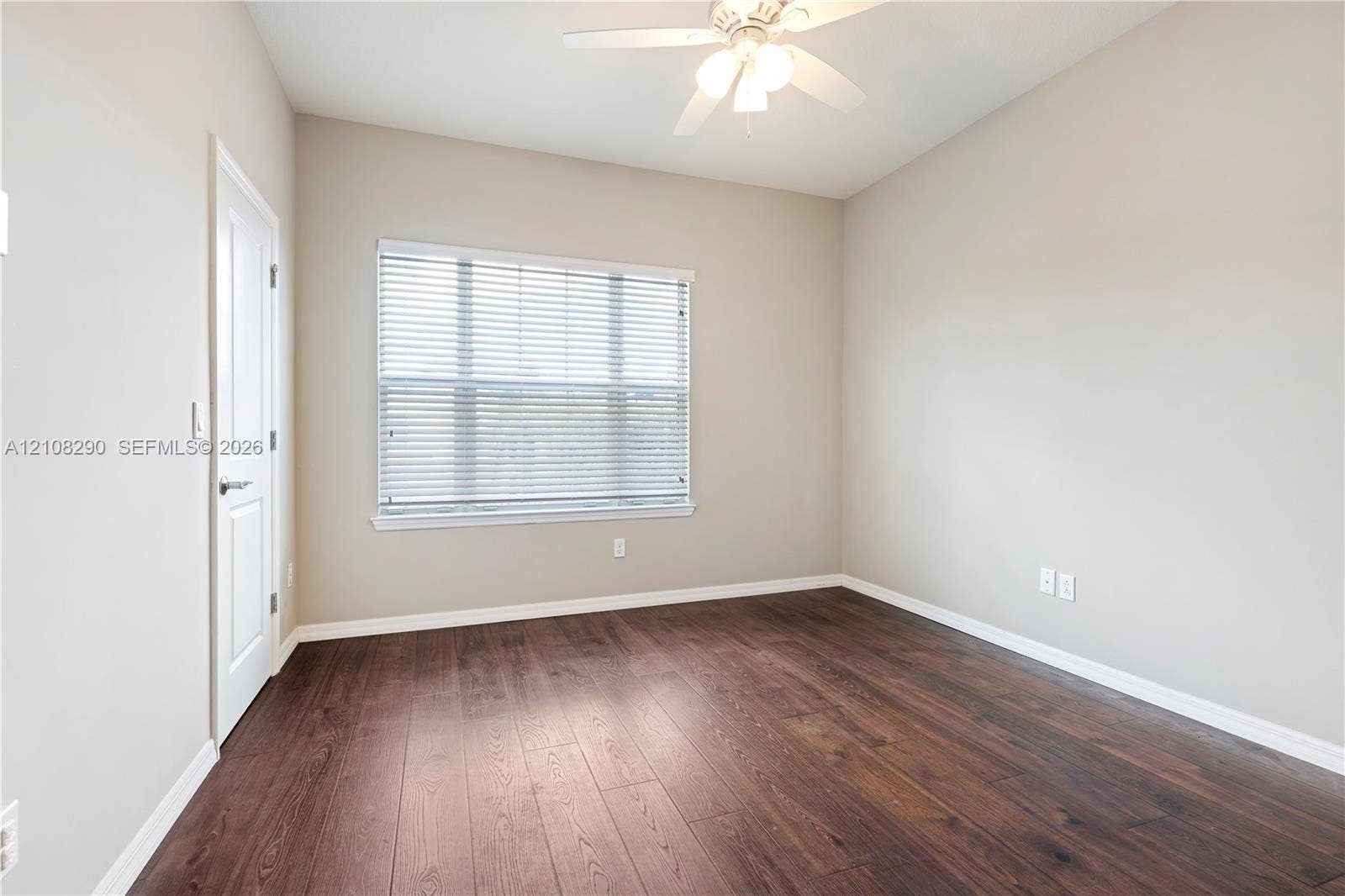 Neutral interior featuring wood-finish flooring, a multi-blade ceiling fan with integrated lighting, and a window with horizontal blinds