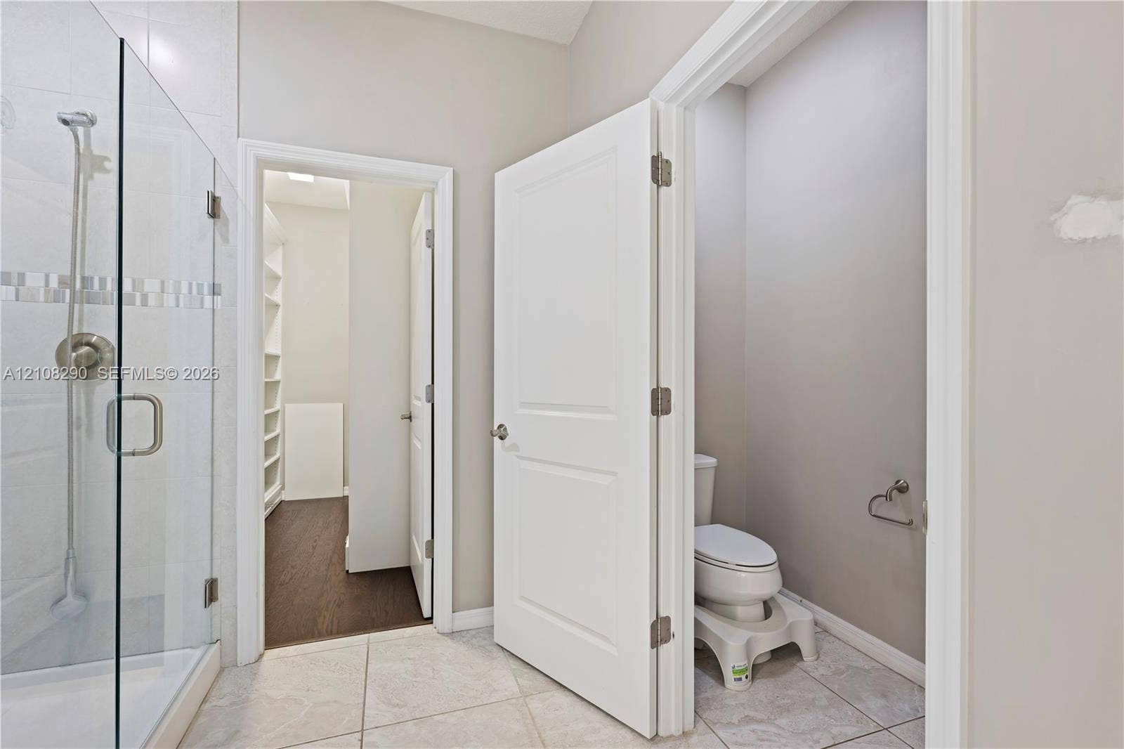 Walk-in shower with a glass enclosure, tile flooring, and a separate water closet featuring a two-panel door
