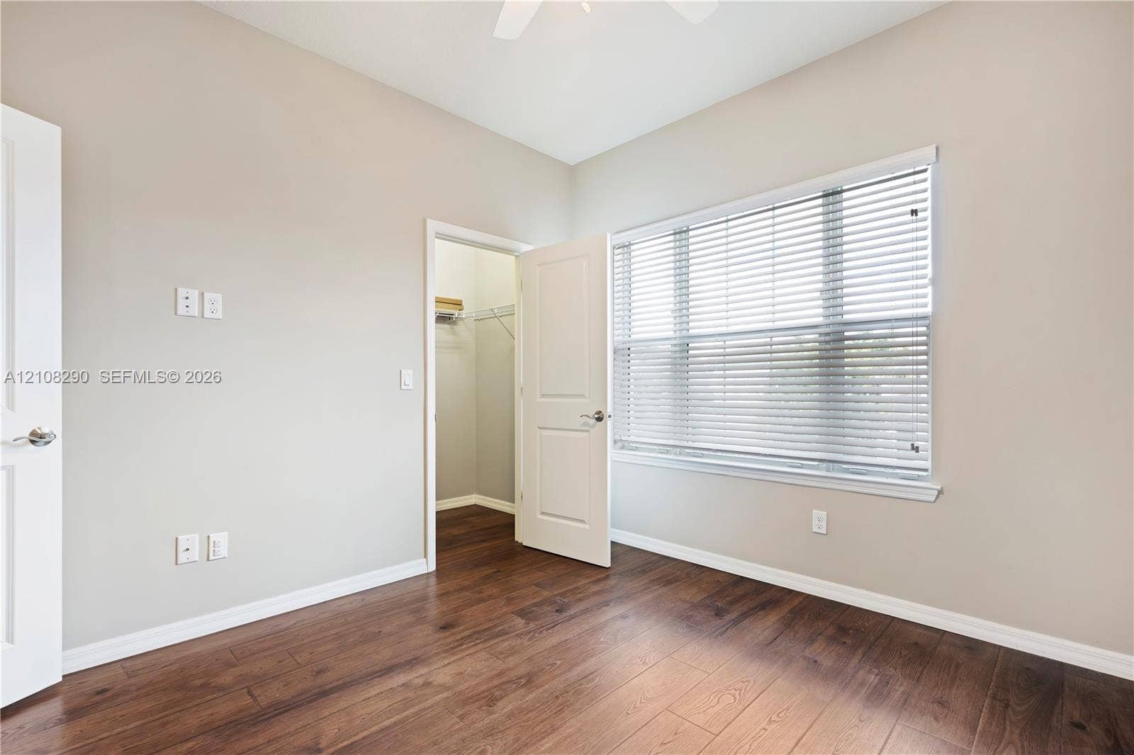 Interior space featuring wood-finish flooring, a neutral wall palette, a walk-in closet, and a window with horizontal blinds