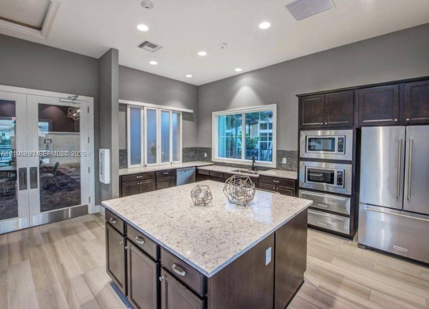 Kitchen featuring a central island with a stone countertop, dark wood cabinetry, stainless steel built-in appliances, recessed lighting, and wood-finish flooring
