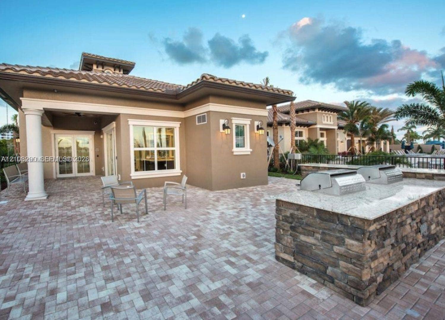 Covered terrace featuring stone paver flooring, outdoor kitchen with stone veneer base and stone countertop, and double-door entry