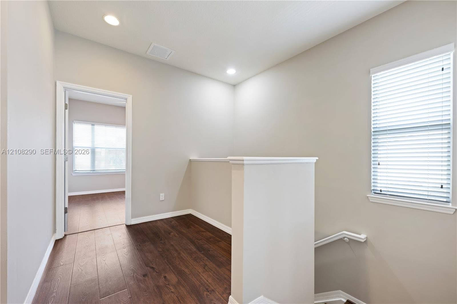 Neutral interior space featuring wood-finish flooring, recessed lighting, and a white handrail