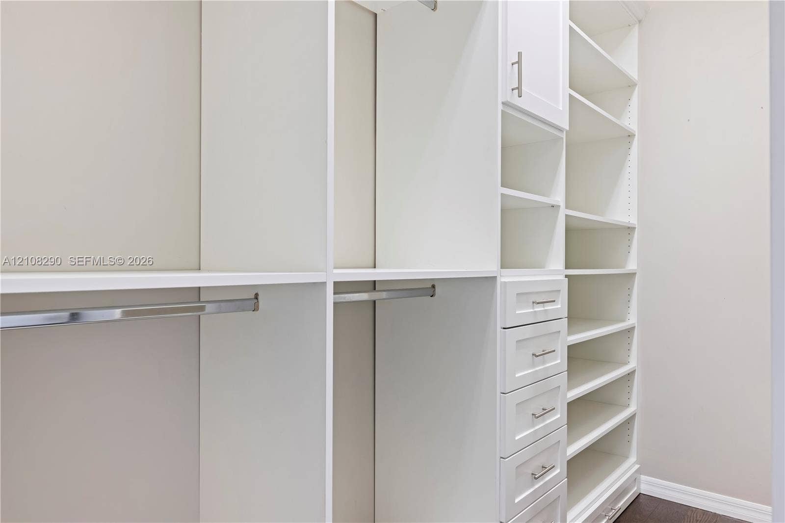 Custom closet featuring floor-to-ceiling white cabinetry, built-in shelving, integrated hanging rods, and a bank of storage drawers with brushed metal pulls