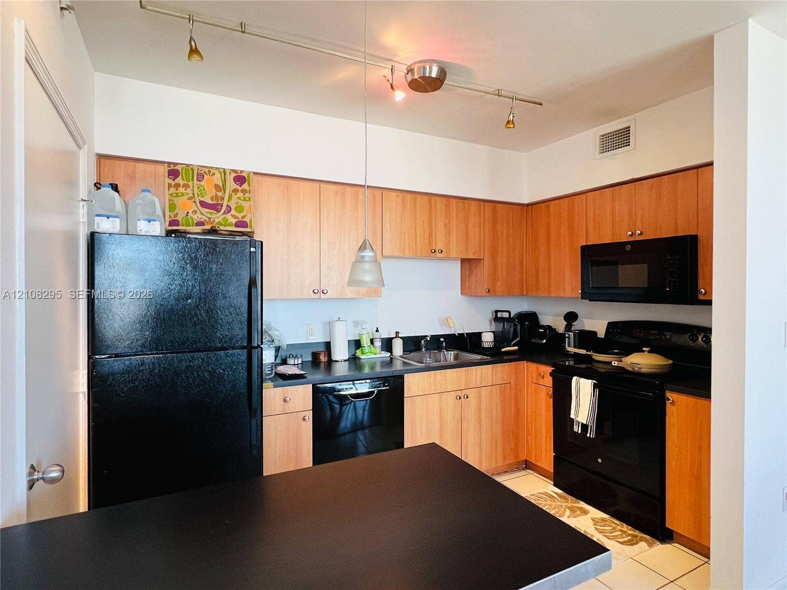 Kitchen featuring wood-finish cabinetry, solid surface countertops, black built-in appliances, and track lighting