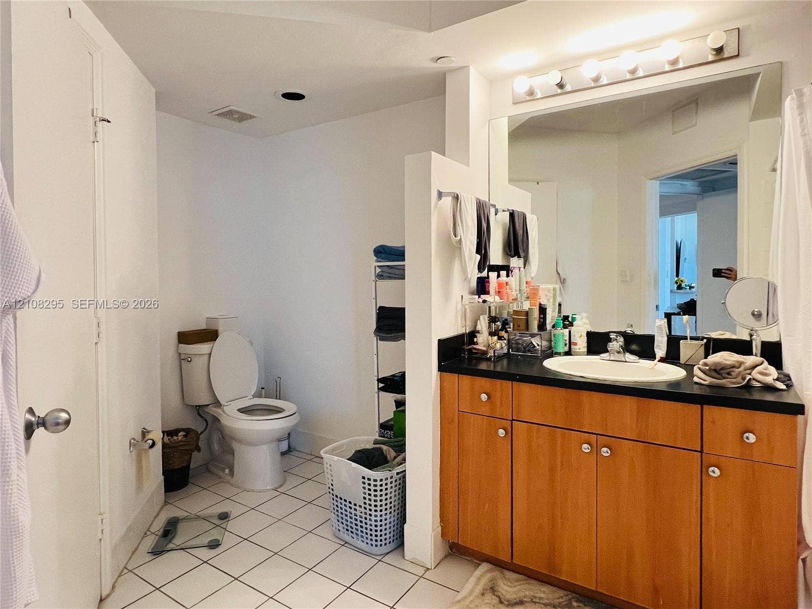 Bathroom featuring a wood-finish vanity with a dark solid-surface countertop, an integrated oval sink, a wall-to-wall mirror, and overhead theater-style lighting