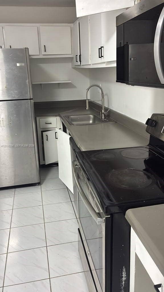 1800 Sans Souci Boulevard, #340, North Miami, North Miami, FL 33181 Kitchen featuring white cabinetry, stainless steel appliances, solid-surface countertops, a stainless steel sink with a high-arch faucet, and tile flooring