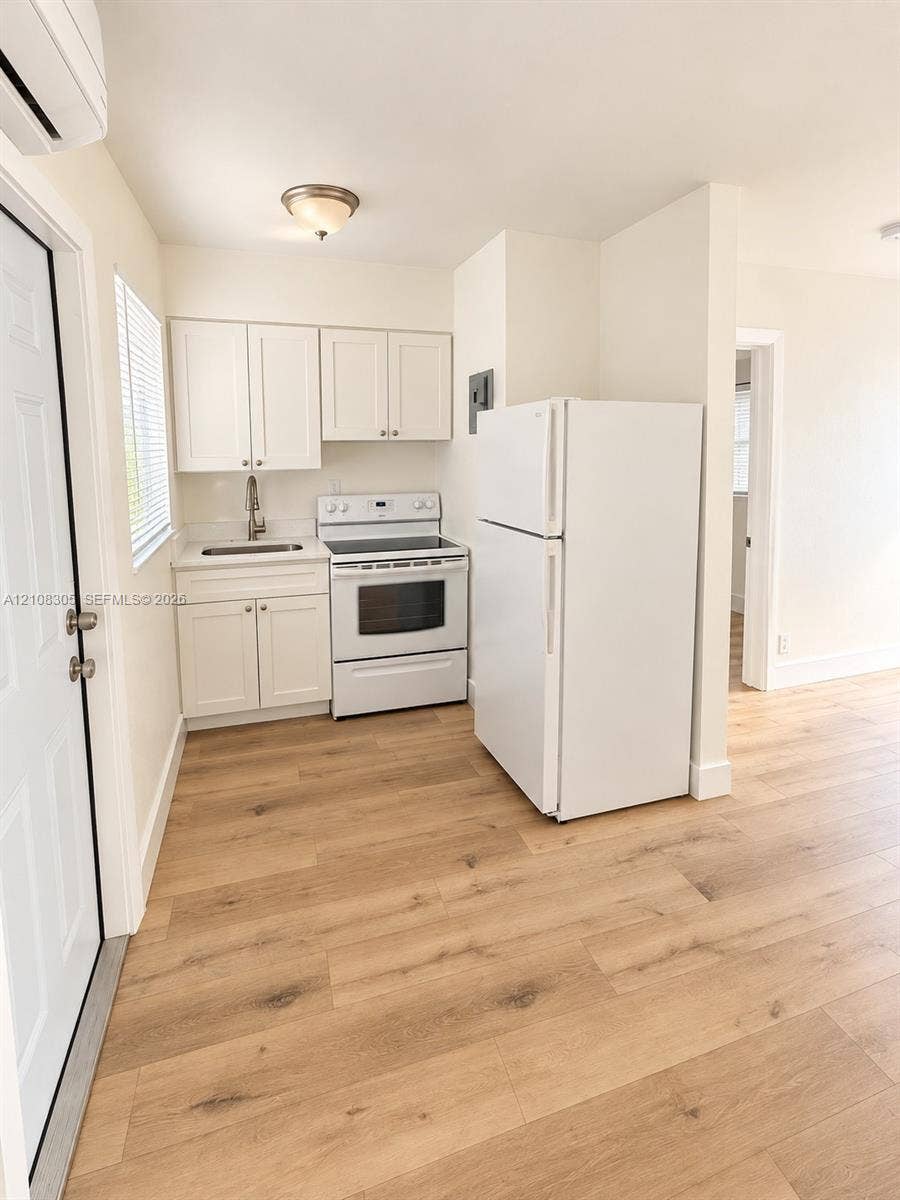 Kitchen featuring white cabinetry, wood-finish flooring, a white electric range, and a drop-in sink