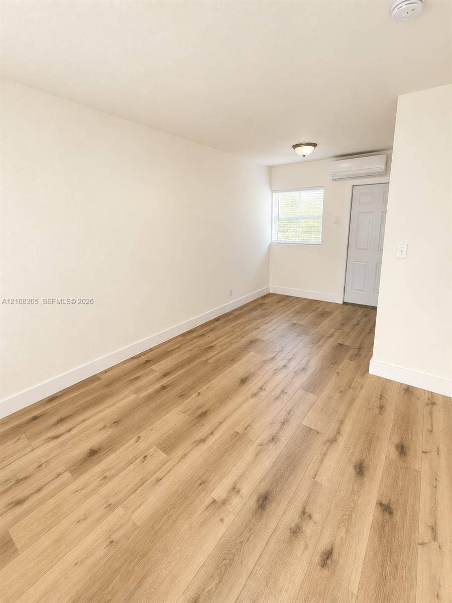 Interior space featuring wood-finish flooring, a wall-mounted ductless climate control unit, a single window with blinds, and a paneled interior door