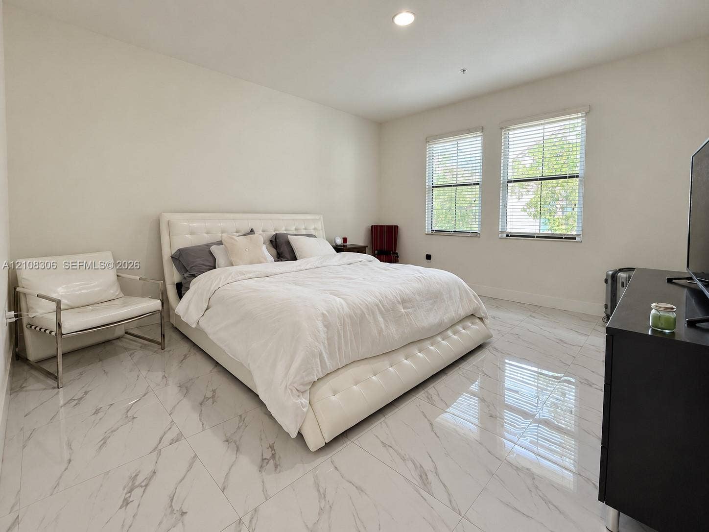 Large-format, polished stone-finish flooring with prominent veining, recessed ceiling lighting, and dual windows with horizontal blinds