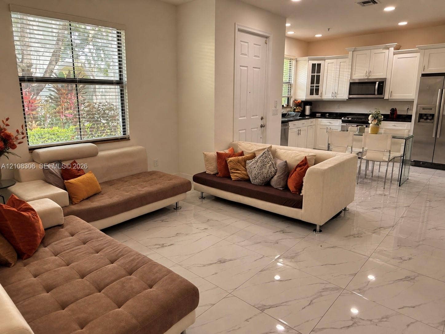 Large-format polished tile flooring, white shaker-style cabinetry, dark countertops, stainless steel appliances, and recessed lighting