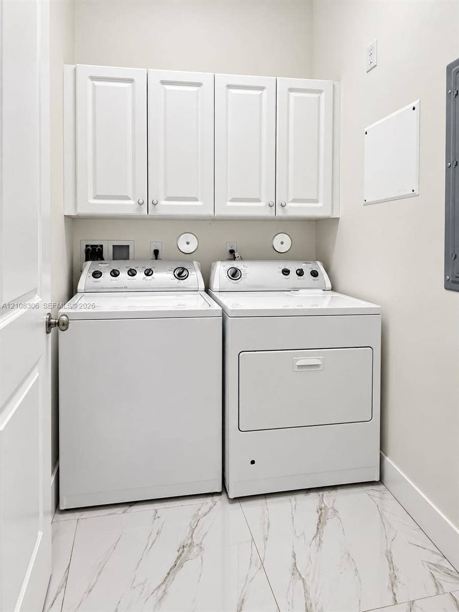 Laundry area featuring white shaker-style wall cabinets, large-format tile flooring with a veined pattern, and dedicated appliance hookups