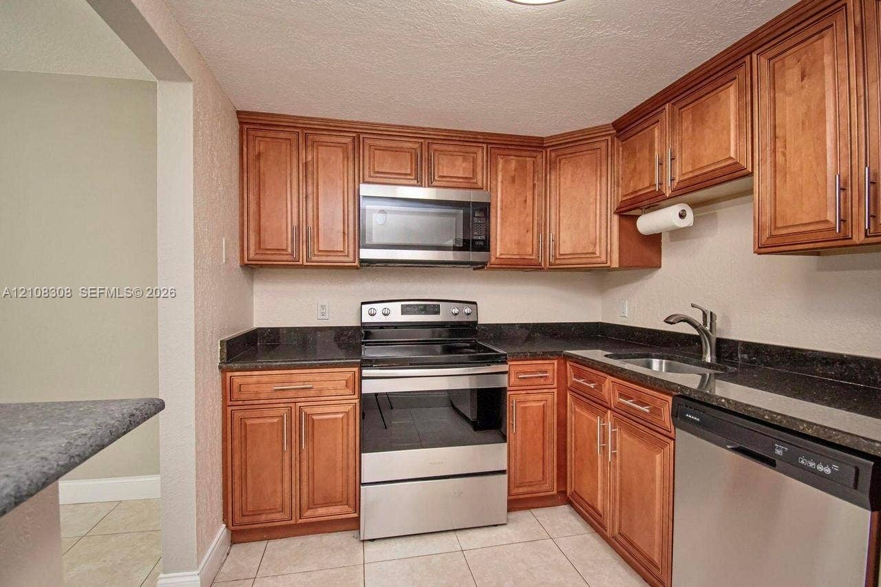 770 SE 2nd Avenue, #E201, Deerfield Beach, FL 33441 Kitchen featuring wood cabinetry, stone-finish countertops, stainless steel appliances, a double-basin sink, and tile flooring