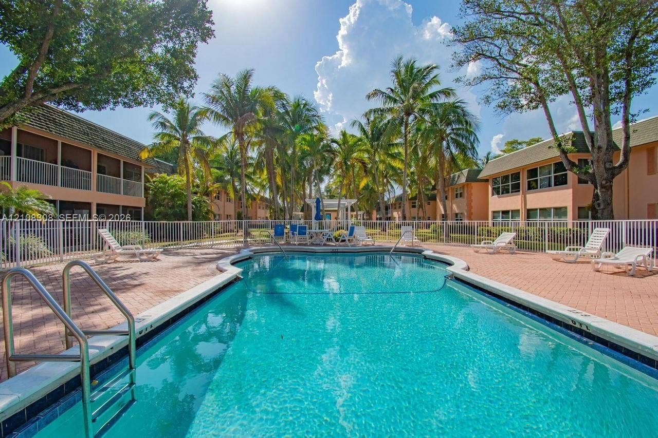 770 SE 2nd Avenue, #E201, Deerfield Beach, FL 33441 Swimming pool with a paved deck, metal perimeter fencing, and mature palm trees