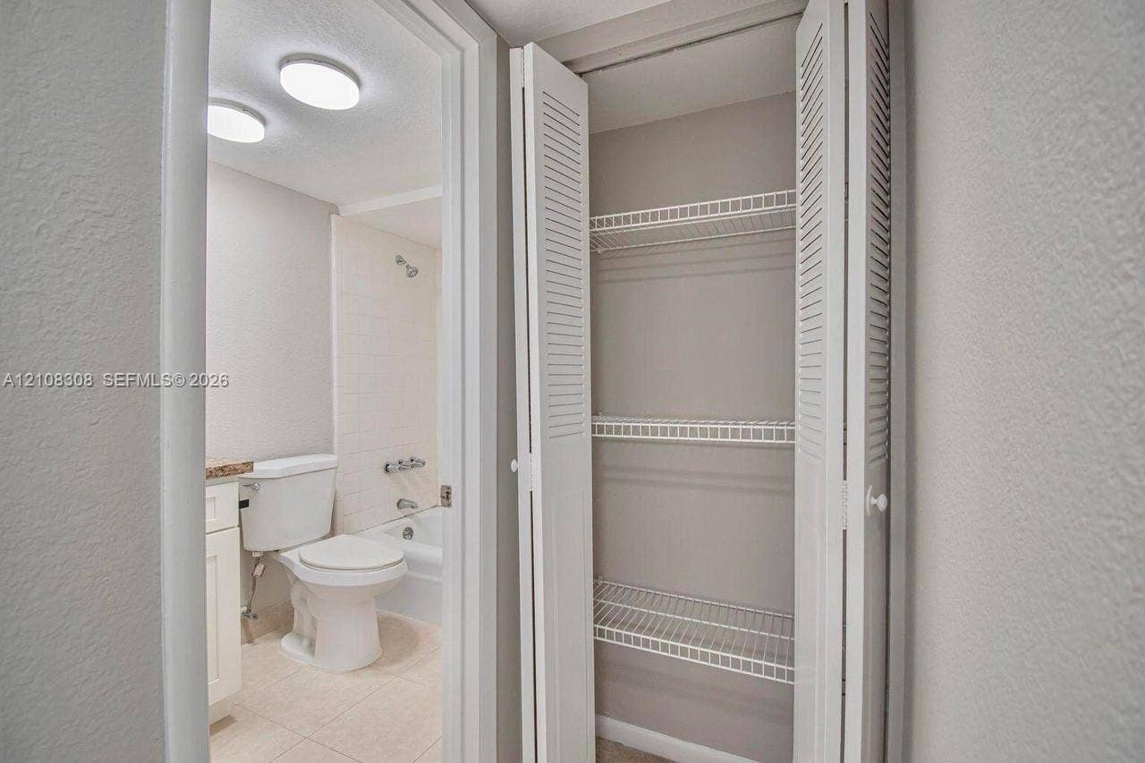 770 SE 2nd Avenue, #E201, Deerfield Beach, FL 33441 Built-in storage closet with louvered bi-fold doors and wire shelving, featuring a tiled bathtub enclosure, porcelain toilet, and recessed ceiling lighting