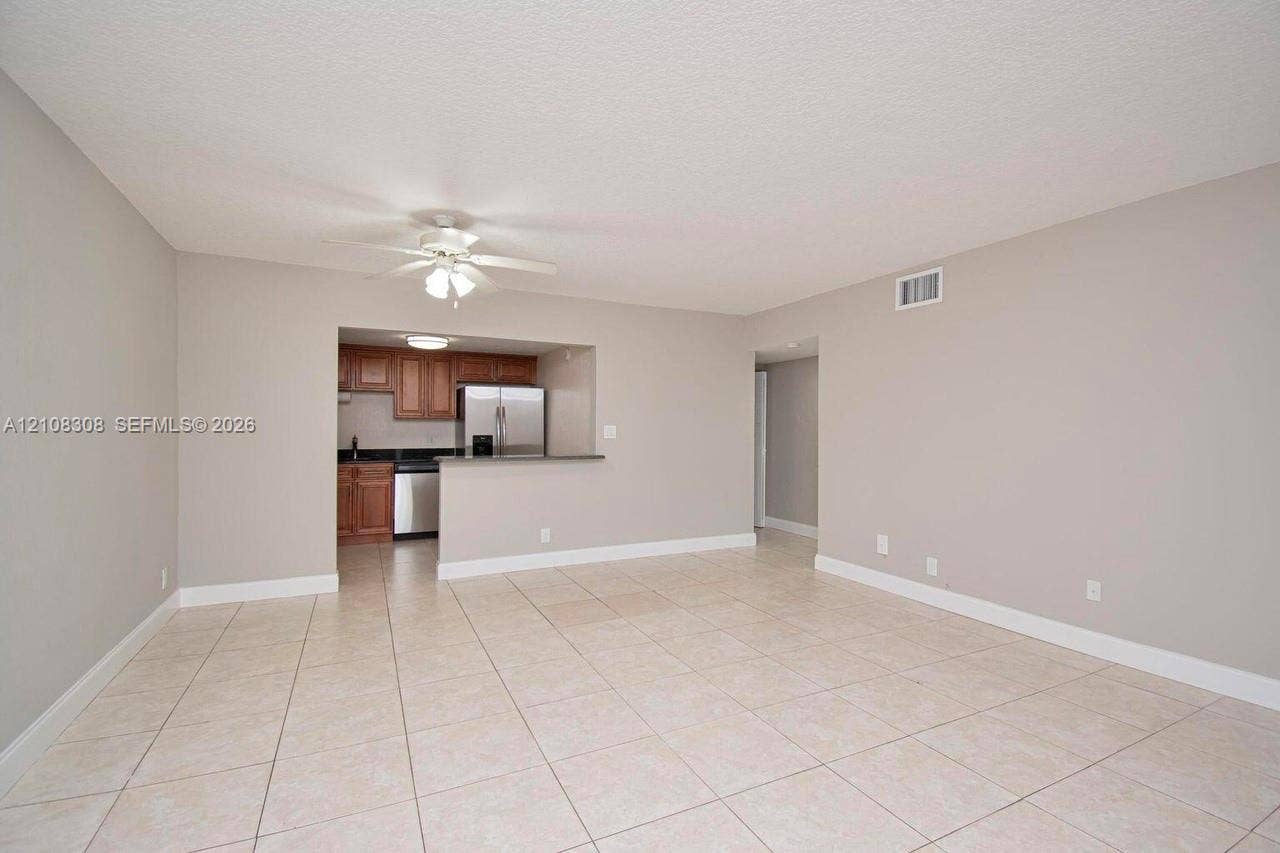 770 SE 2nd Avenue, #E201, Deerfield Beach, FL 33441 Open living area featuring neutral wall paint, tile flooring, a ceiling fan with light kit, and a kitchen pass-through with a peninsula