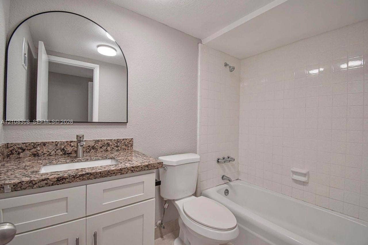 770 SE 2nd Avenue, #E201, Deerfield Beach, FL 33441 White cabinetry with stone-finish countertop, arched wall mirror, and tiled shower-tub combination