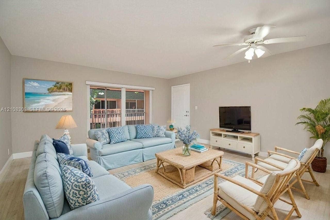 770 SE 2nd Avenue, #E201, Deerfield Beach, FL 33441 Living area featuring wood-finish flooring, a ceiling fan with integrated lighting, and a large sliding glass door with horizontal blinds