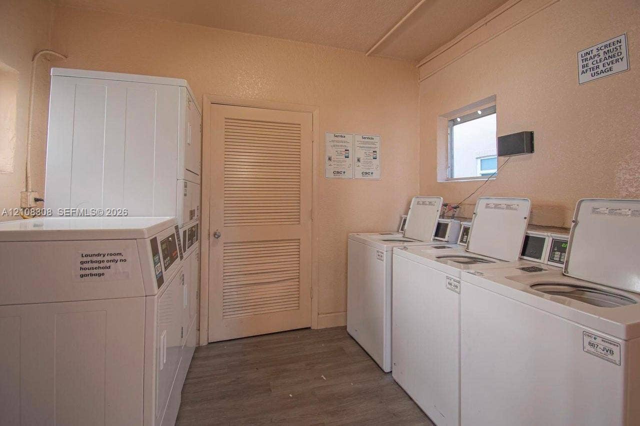 770 SE 2nd Avenue, #E201, Deerfield Beach, FL 33441 Laundry facility featuring multiple top-load washers, a stackable dryer unit, louvered interior door, and wood-finish flooring