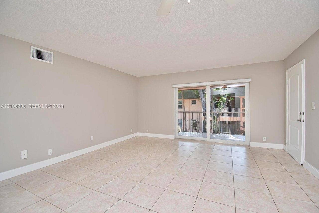 770 SE 2nd Avenue, #E201, Deerfield Beach, FL 33441 Neutral-toned interior space featuring ceramic tile flooring, sliding glass patio doors, and a ceiling-mounted fan