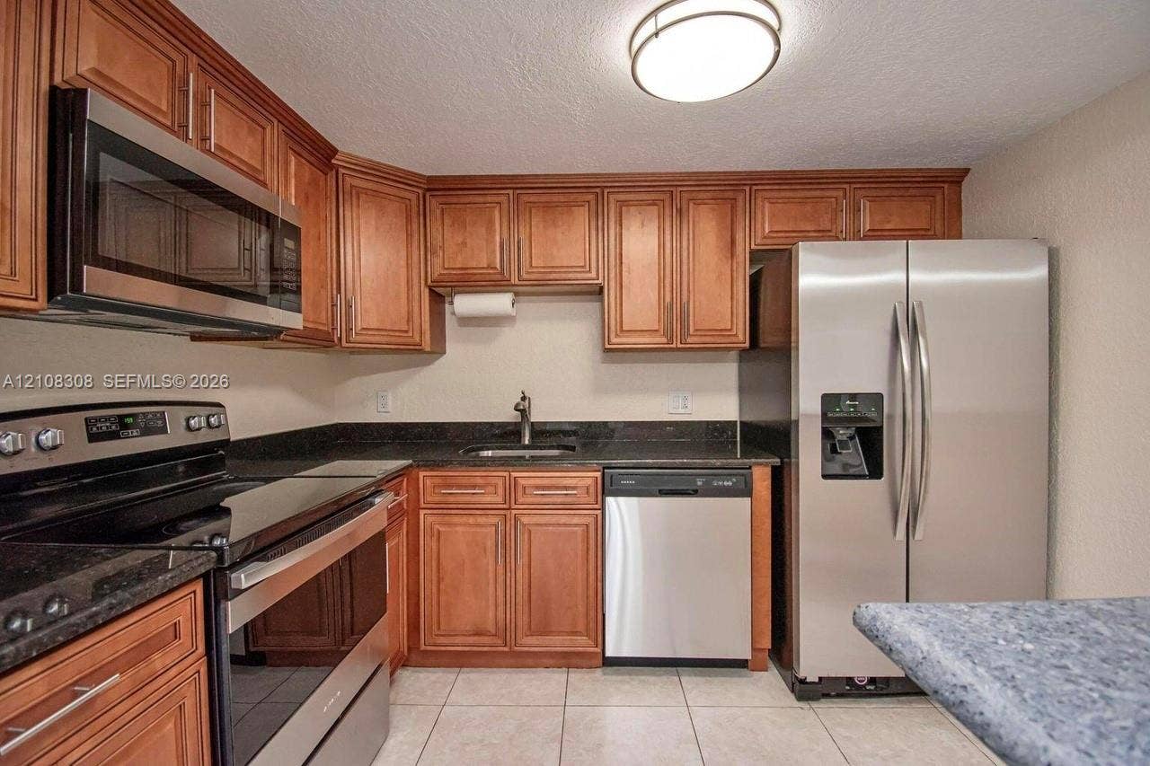 770 SE 2nd Avenue, #E201, Deerfield Beach, FL 33441 Kitchen featuring wood cabinetry, stone-surface countertops, tile flooring, and stainless steel appliances