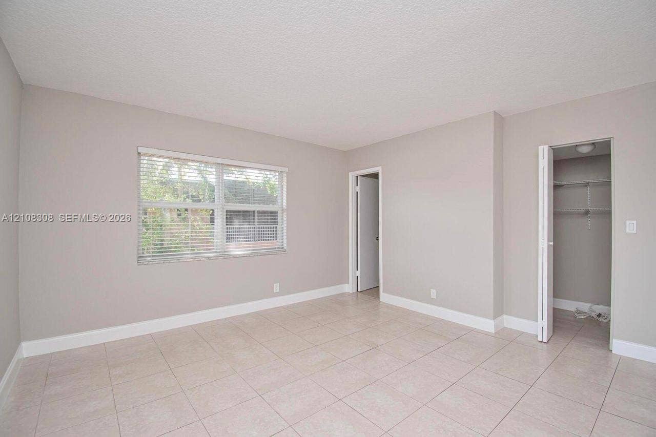 770 SE 2nd Avenue, #E201, Deerfield Beach, FL 33441 Neutral-toned interior featuring large-format tile flooring, a dual-pane window with adjustable blinds, and a built-in closet with folding doors and wire shelving