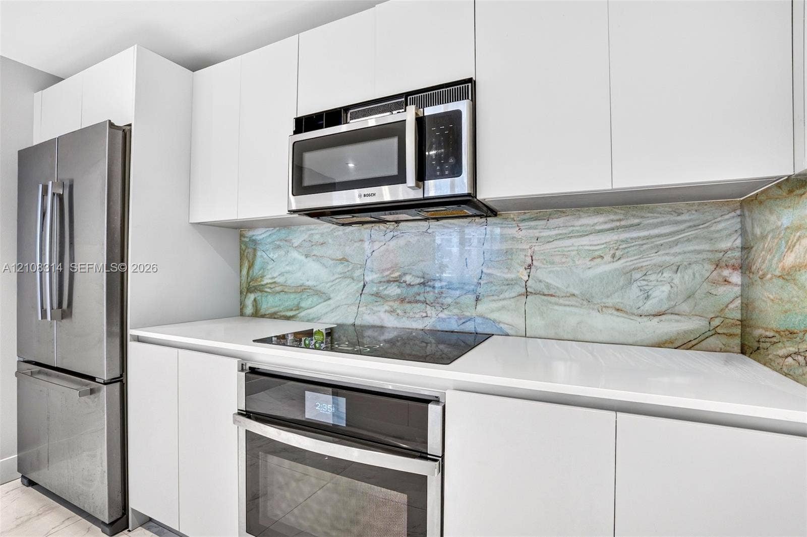 488 NE 18th Street, #4010, Miami, FL 33132 Kitchen featuring flat-panel white cabinetry, stone-patterned slab backsplash, quartz countertops, and stainless steel appliances including a built-in oven, electric cooktop, and over-the-range microwave