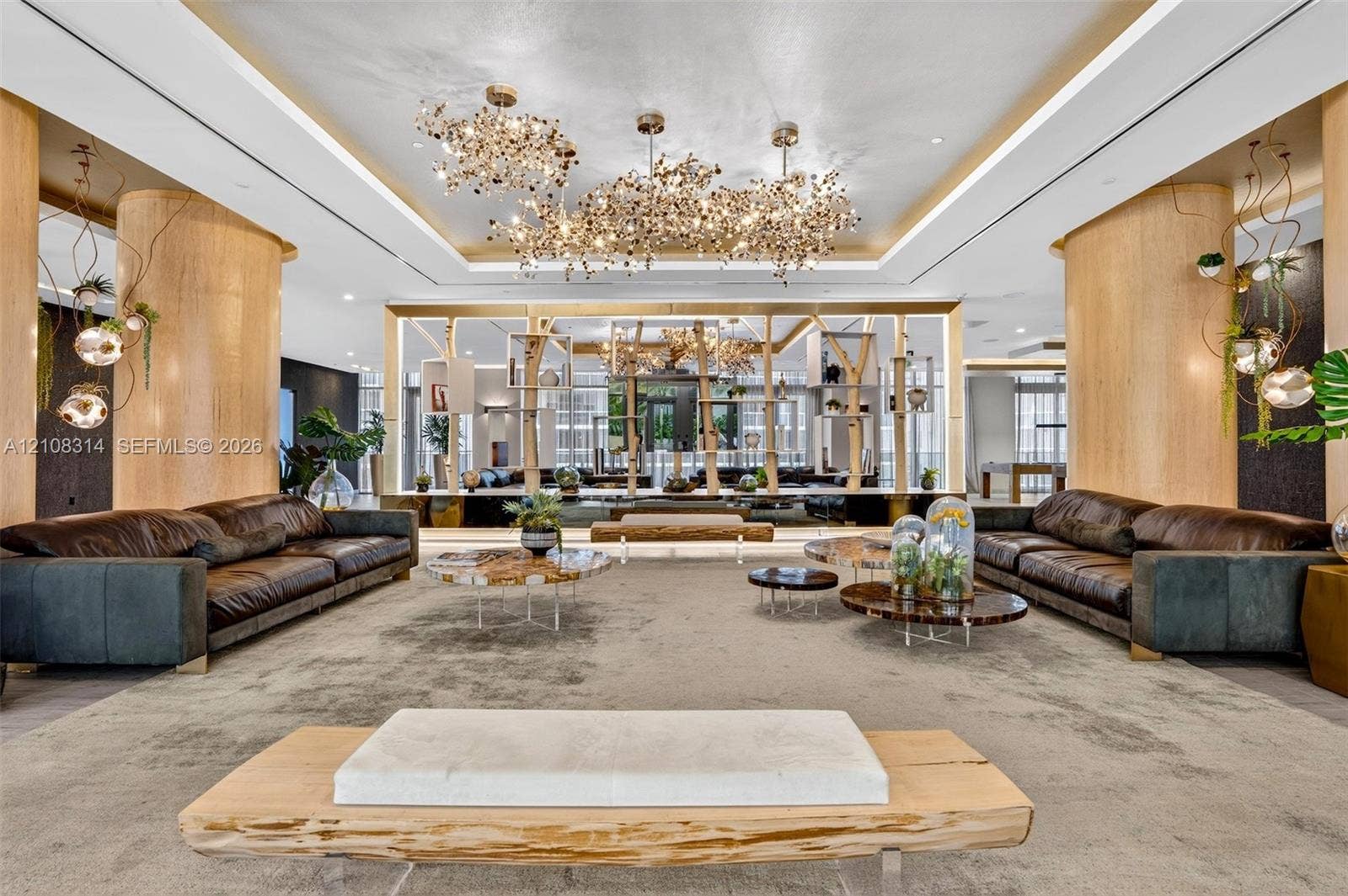 488 NE 18th Street, #4010, Miami, FL 33132 Expansive room featuring cylindrical wood-finished support columns, custom multi-cluster decorative chandeliers, recessed tray ceiling lighting, and a floor-to-ceiling built-in geometric wood-frame partition